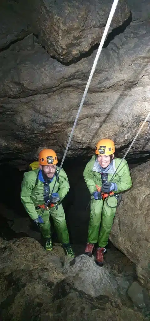 Un couple équipé d'une tenue de spéléologie d'un casque et d'une lampe frontale descend en rappel cote à cote dans le Puits des Bans