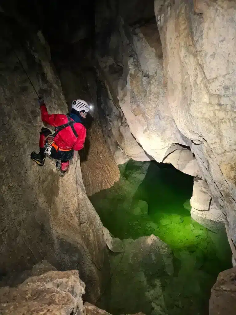 Un spéléologue descend en rappel et éclaire avec sa lampe frontale le lac souterrain lors d'une sortie de spéléologie à Céüse