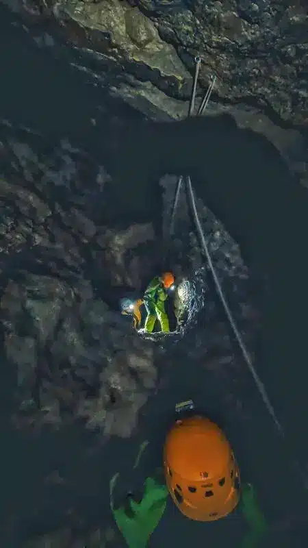 Un spéléologue éclaire devant lui une personne qui descend en rappel dans le Puits des Bans