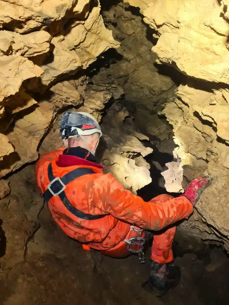 Un spéléologue équipé d'une combinaison orange et d'un casque assis regarde le meandre d'une rivière souterainne