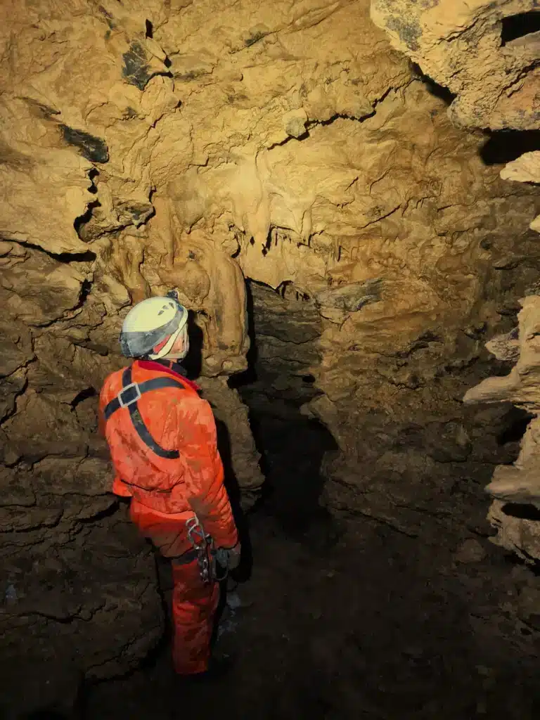 Une personne équipée en tenue de spéléologie regarde des stalactites suspendue au plafond de la grotte de SuperDévoluy