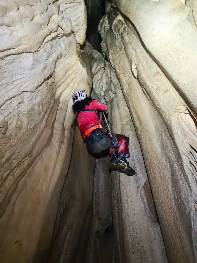 Une personne remonte sur une corde pour escalader un puits d'une grotte naturelle, sa lampe frontale installée qur son casque éclaire le plafond