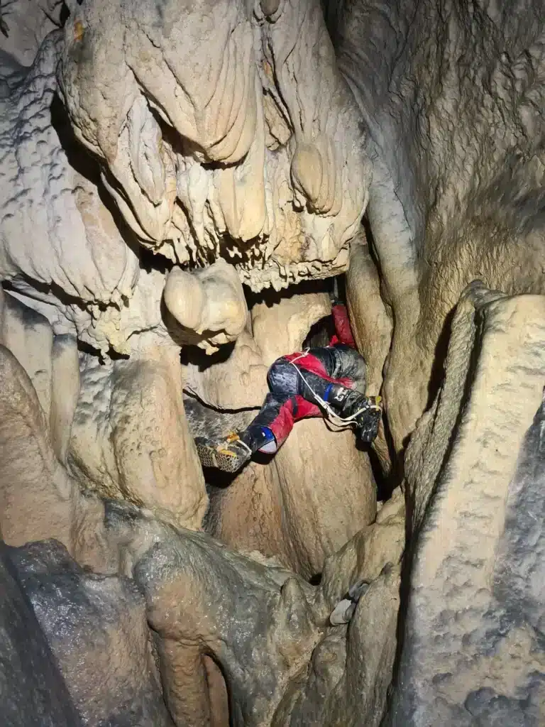 Vue sur les pieds d'un spéléologue qui franchit un passage étroit entre les stalactites