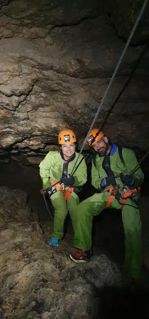 deux personnes en tenue de spéléologie descendent à l'un à coté de l'autre en rappel à l'aide de cordes et d'un harnais de sécurité