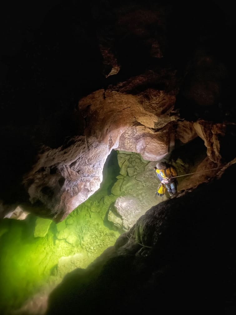 un spéléologue descend en rappel à l'aide d'une corde et éclaire le lac souterrain qui se trouve en dessous