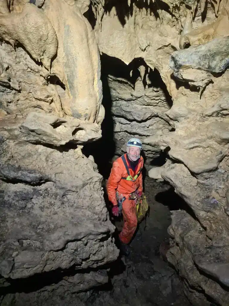 un spéléologue équipé d'un casque, d'une lampe frontale, et dune combinaison de spéléologie regarde des stalactites
