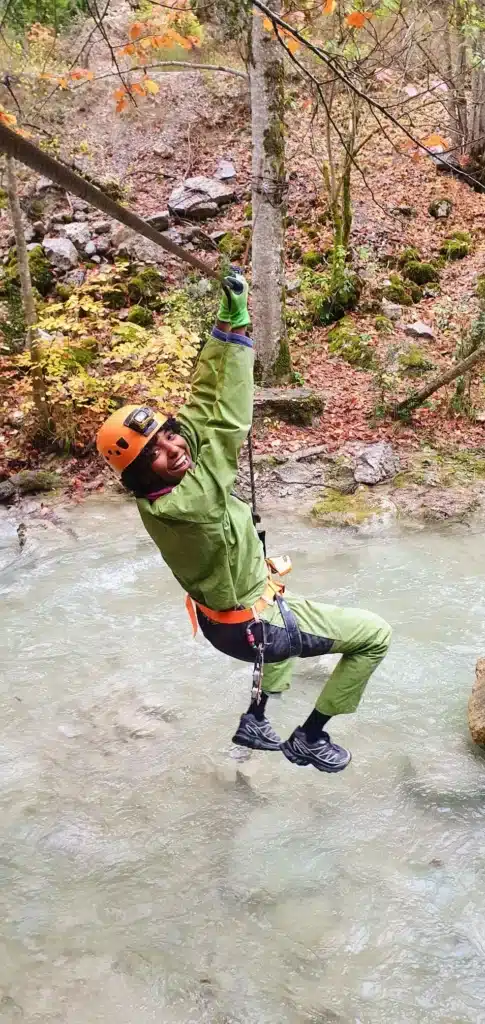 une personne en tenue de spéléologie traverse la rivière des gorges d'Agnielles en tyrolienne