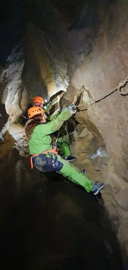 une personne équipée d'un casque d'une lampe frontale et d'un baudrier progresse sur une main courante dans la grotte de la Résurrection dans les gorges d'Agnielles
