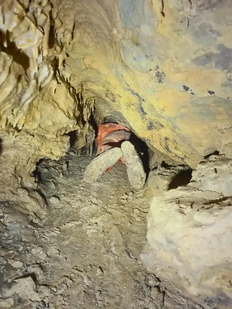 vue sur les jambes d'un spéléologue qui essaie de franchir un passage étroit
