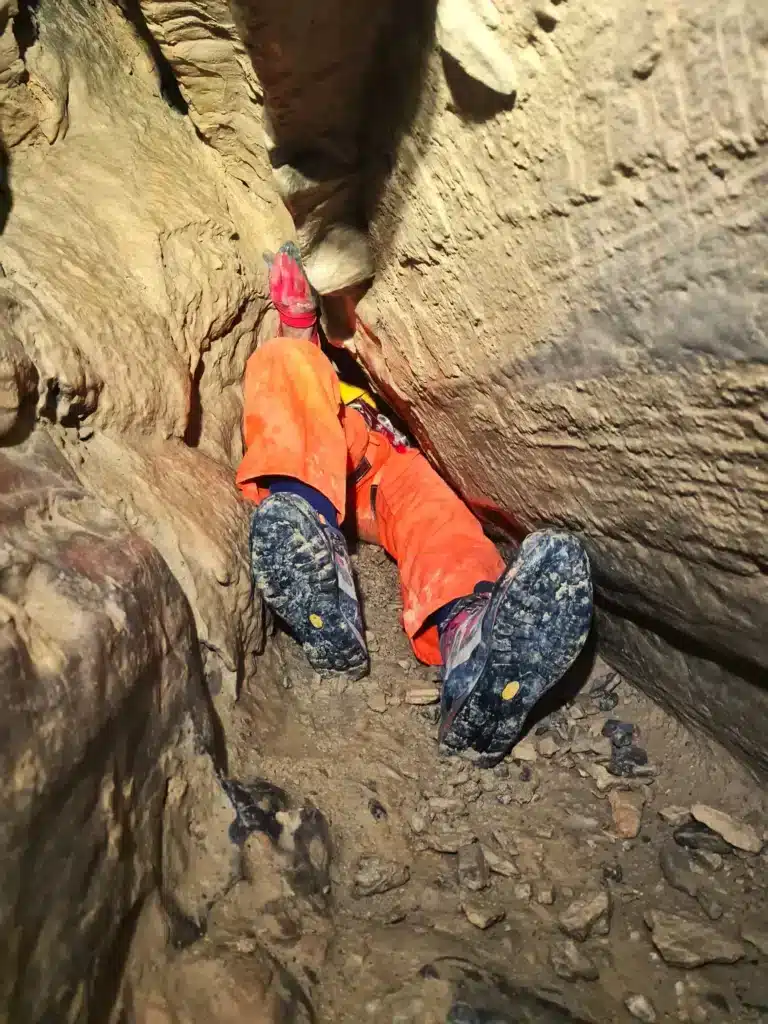 vue sur les pieds d'une personne qui essaie de franchir un boyau de spéléologie à SuperDévoluy