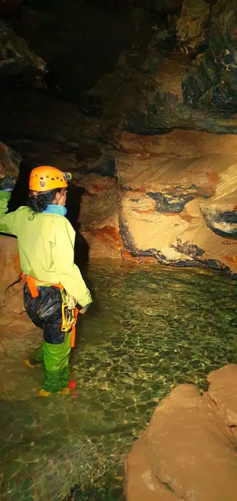 Une personne équipée d'une tenue de spéléologie éclaire le siphon du Puits des Bans