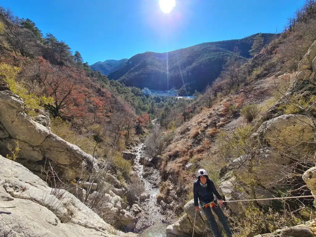 Une personne équipée d'un casque et d'un baudrier descend dans une cascade d'un canyoning à Orpierre