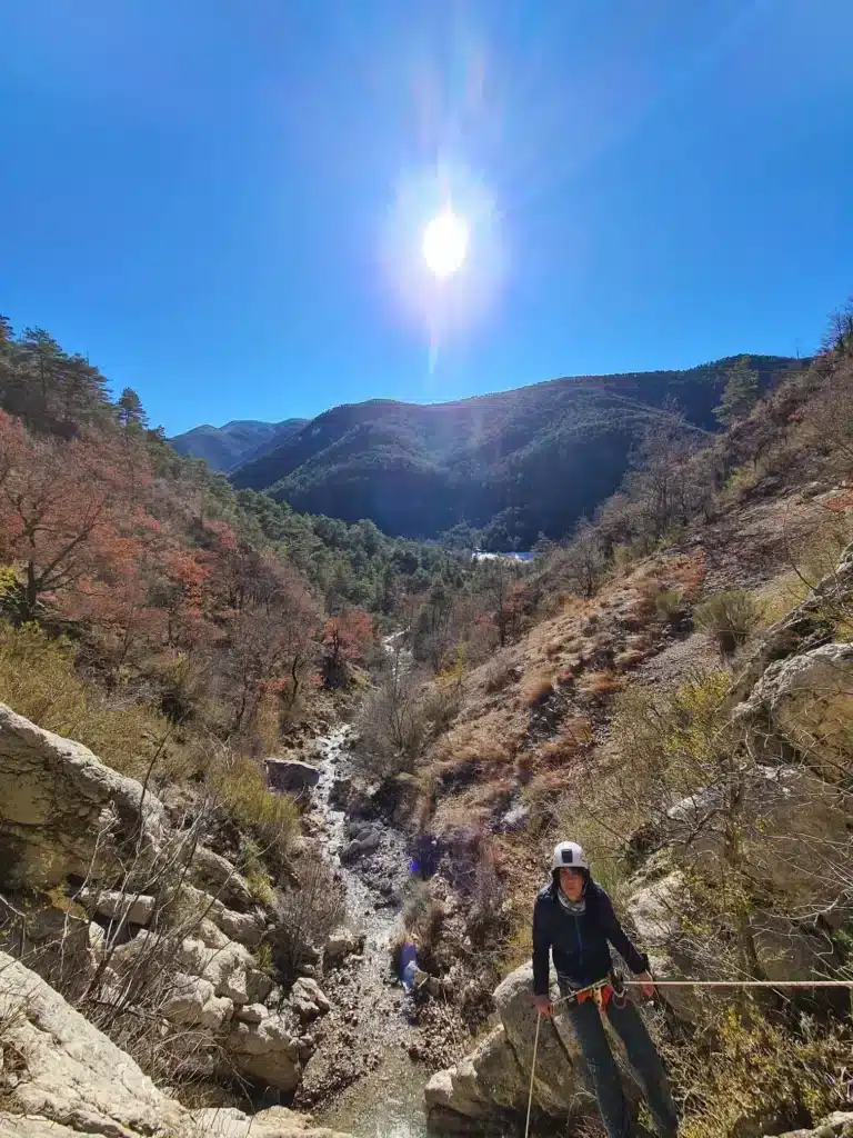 Une personne équipée d'un harnais et d'un casque se sécurise à l'aide d'une corde pour descendre une cascade en canyoning à Orpierre