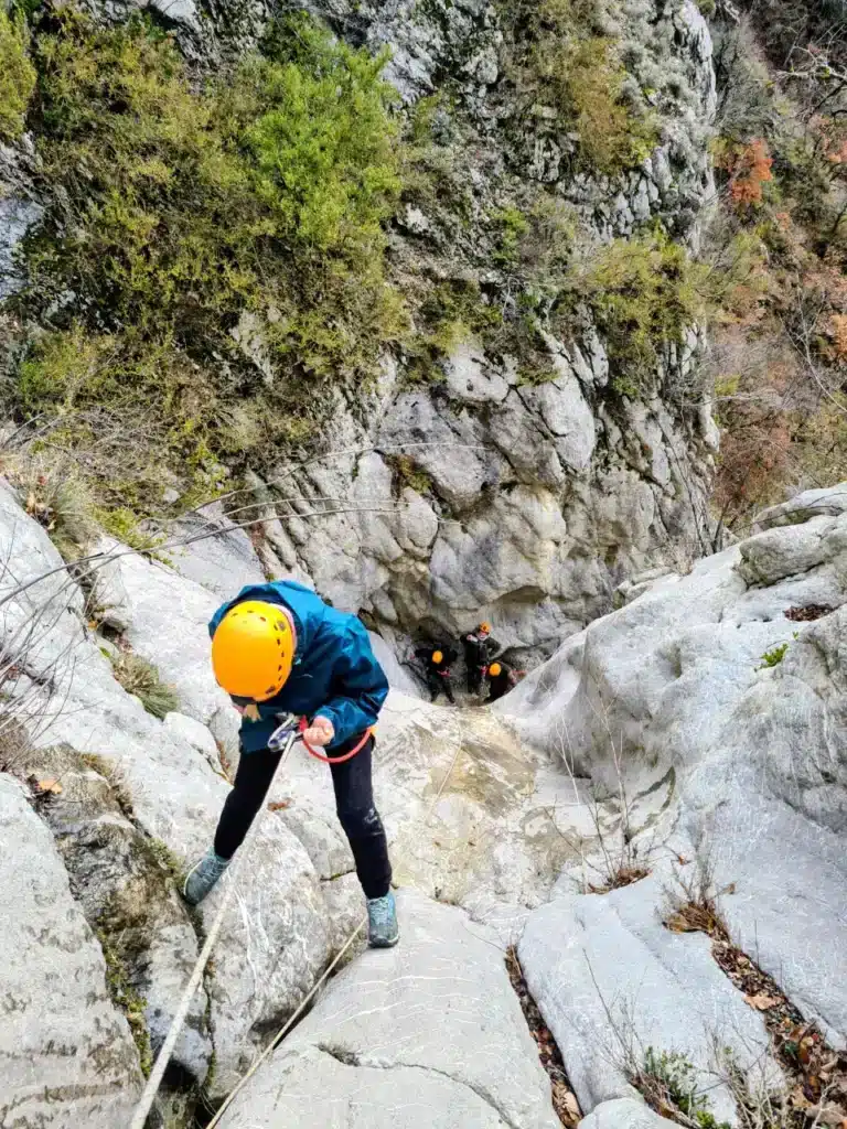 Personne en casque jaune descendant en rappel une paroi rocheuse, d'autres personnes équipées en arrière-plan dans un canyoning proche de Orpierre.