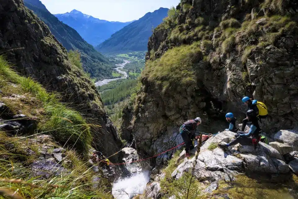 Groupe de personnes équipées en train de faire du canyoning, descendant une cascade dans une vallée montagneuse pour étudier la formation des canyons