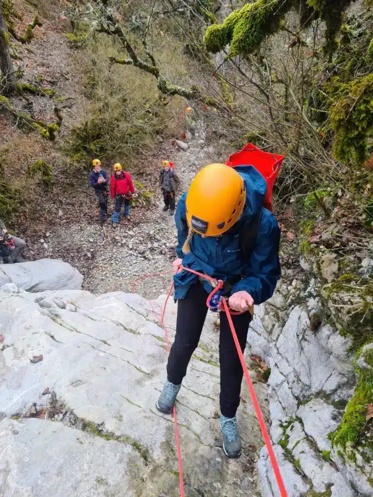 Une personne en casque orange descend en rappel une paroi rocheuse, entourée d'autres participants d'une sortie de canyoning à Rosans.