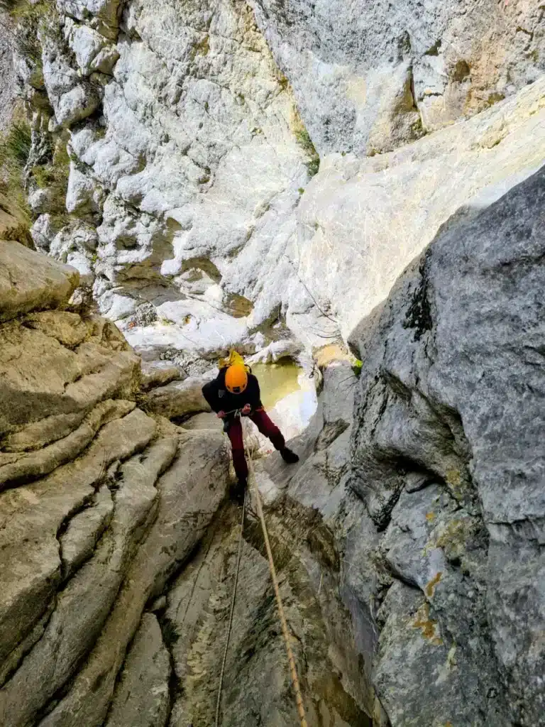 Une personne casquée descend en rappel un canyon rocheux, avec une corde tendue et une petite flaque d'eau en contrebas à Rosans.