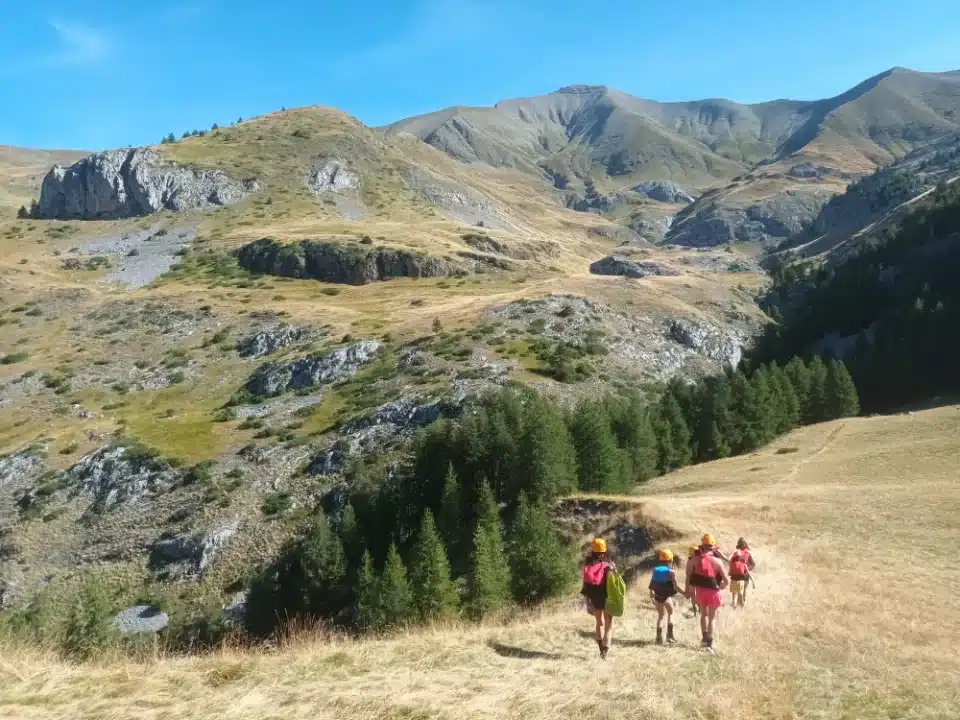 Groupe d'enfants en randonnée dans un paysage montagneux ensoleillé, vêtus de casques et de sacs à dos, étudient la formation des canyons Ancelle