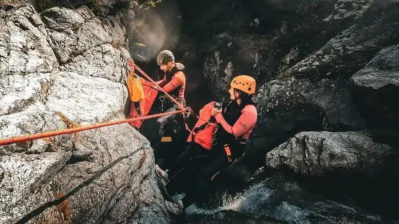 Deux personnes équipées pour le canyoning descendent en rappel dans un canyon à Orcières Merlette, entourées de végétation et d'eau.