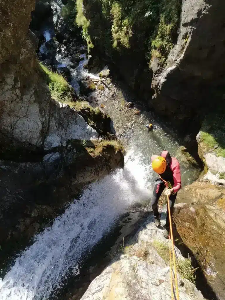 Une personne équipée d'un casque et d'une combinaison descend une cascade en canyoning à proximité de Orcières Merlette, Il est maintenue par une corde.
