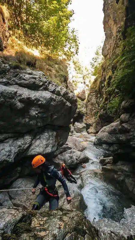 Deux personnes en combinaison néoprène et casque orange font du canyoning à Orcières Merlette, dans un torrent rocheux et étroit en montagne.