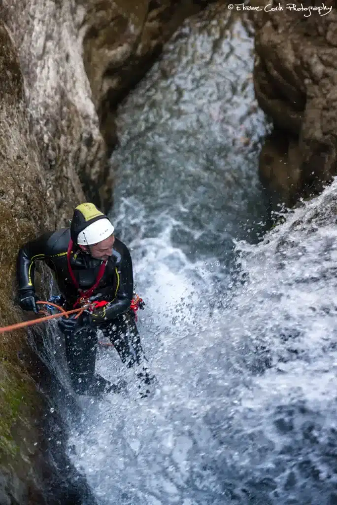 Un homme en combinaison de néoprène et casque descend en rappel une cascade dans le canyon de Rouanette intégrale à Ancelle.