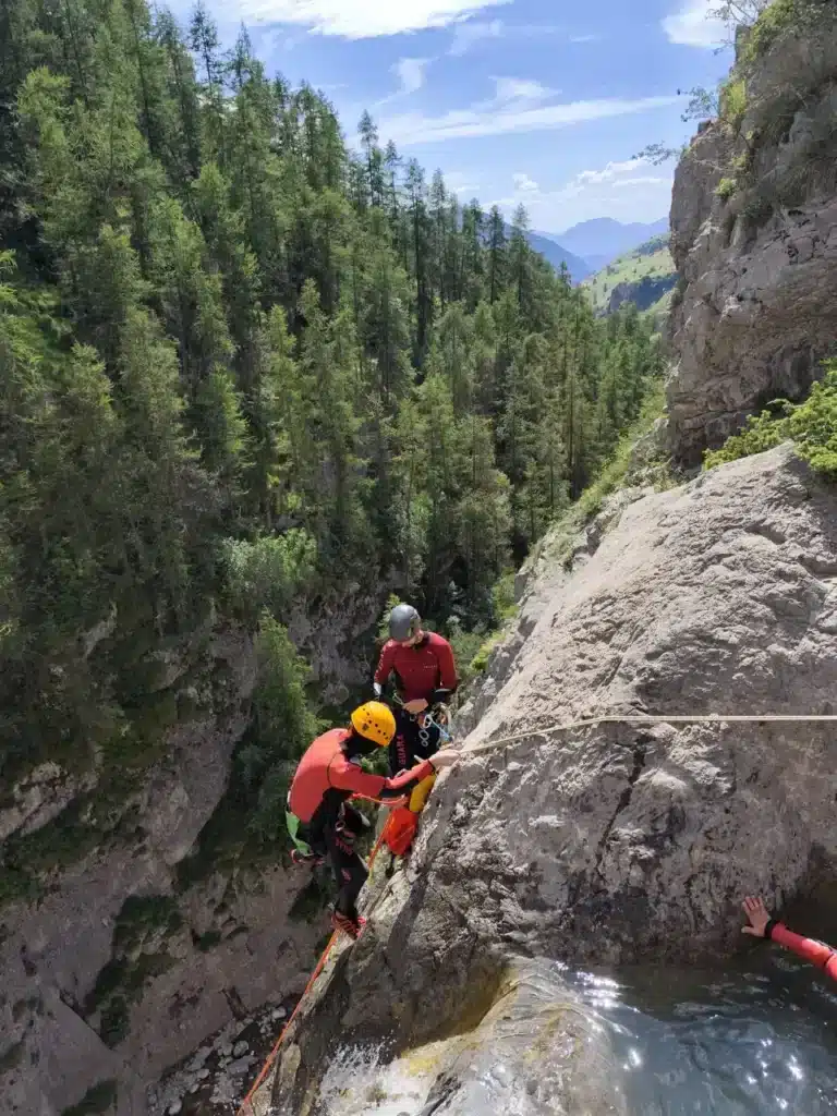 Deux personnes équipées pour le canyoning descendent un rocher escarpé avec une corde du haut de la cascade de Peyron Roux.