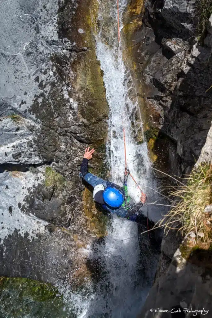 Une personne descend une cascade en rappel, vêtue d'une combinaison bleue et d'un casque bleu, dans le canyon de Rouanette intégrale à Ancelle.