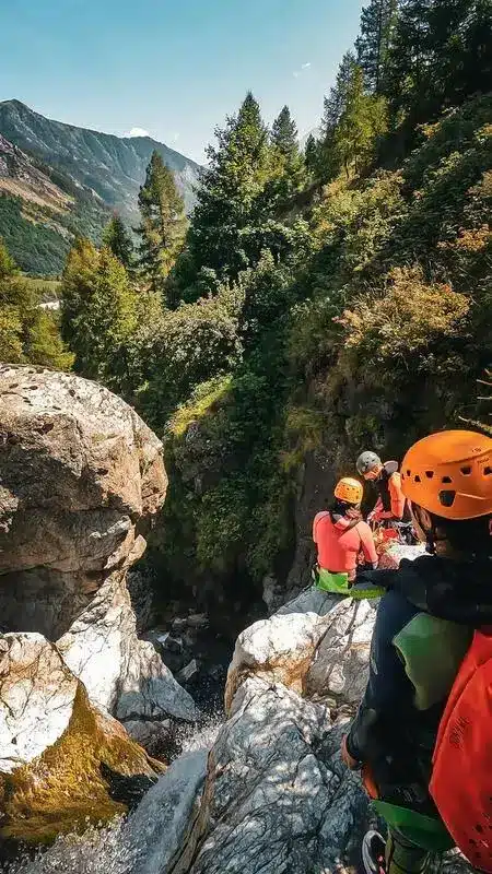 Groupe de personnes équipées pour le canyoning au bord d'une cascade rocheuse en montagne, sous un ciel bleu proche de la station de ski d'Orcières Merlette.