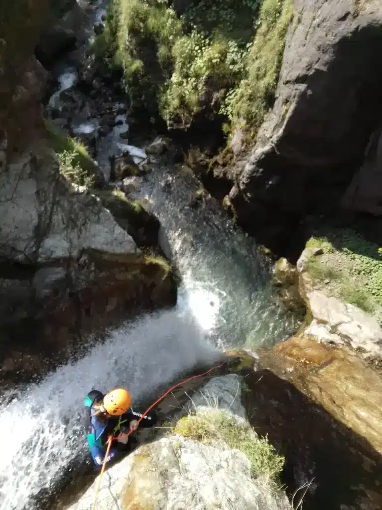 Une personne en équipement de canyoning descend une cascade en utilisant une corde, entourée par la roche et la végétation à Orcières Merlette.