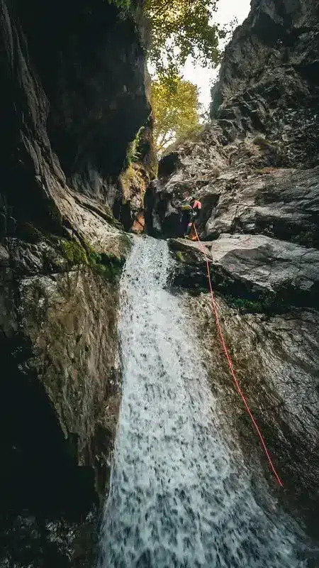 Une personne descend une cascade en rappel dans un canyon à Orcières Merlette, la corde rouge est visible.