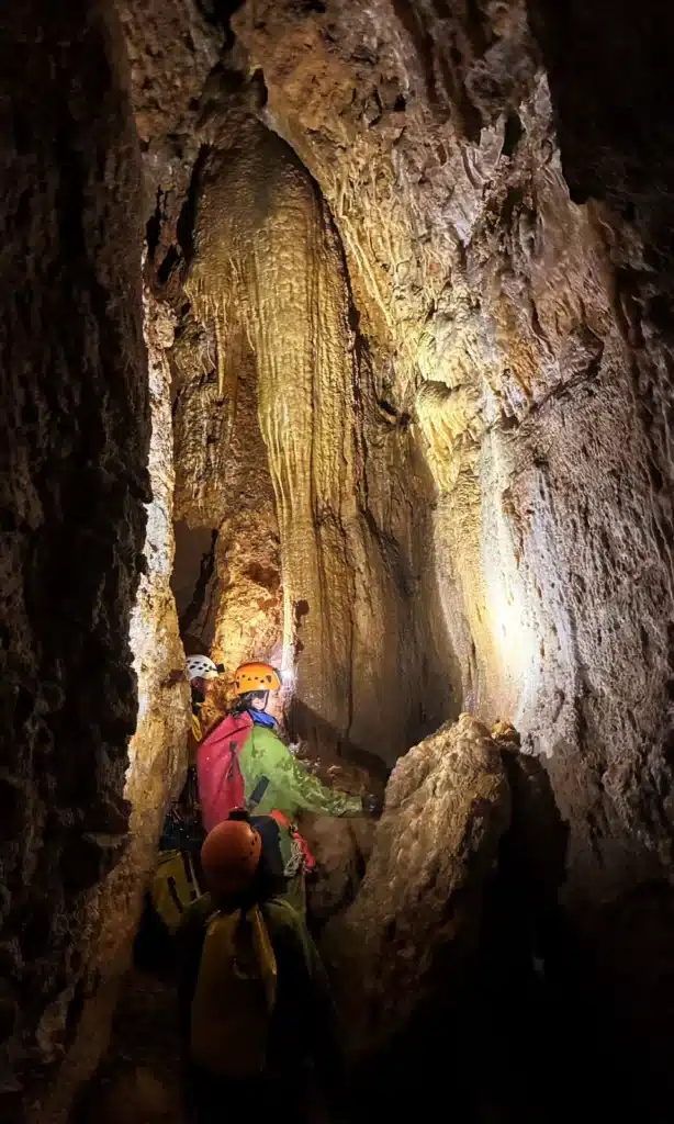 Deux spéléologues équipés de casques et de lampes frontales explorent une grotte du Dévoluy aux formations rocheuses impressionnantes, dont une grande stalactite.