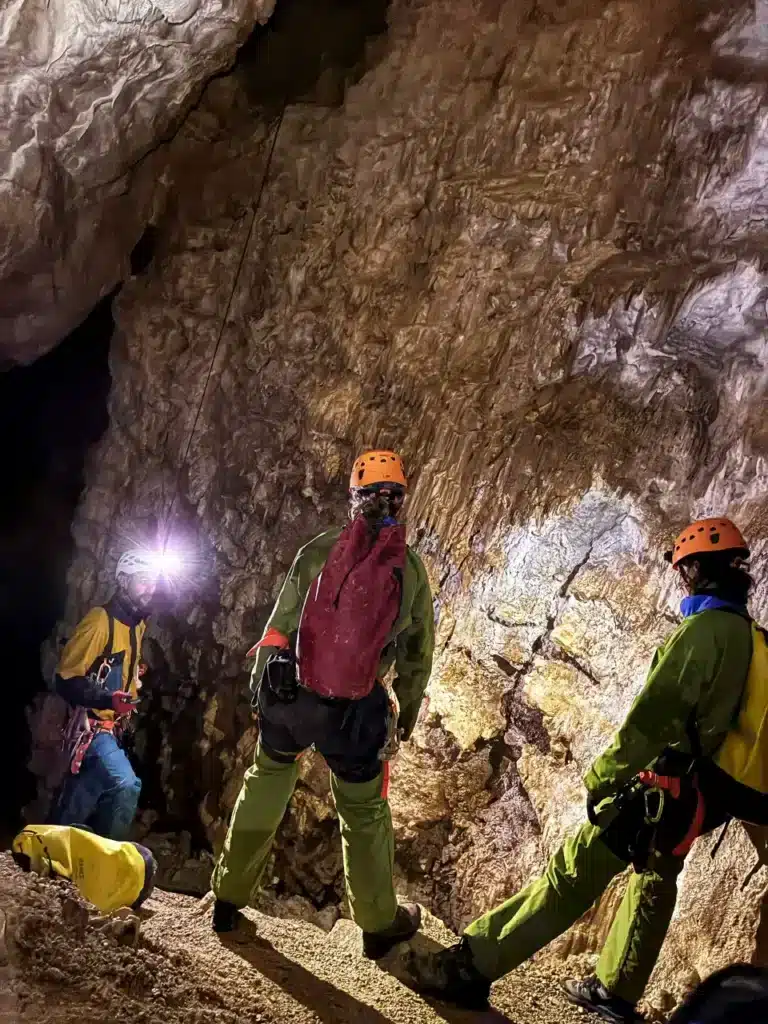 Trois spéléologues équipés de casques et de lampes frontales explorent une grotte des Hautes-Alpes aux formations rocheuses complexes.