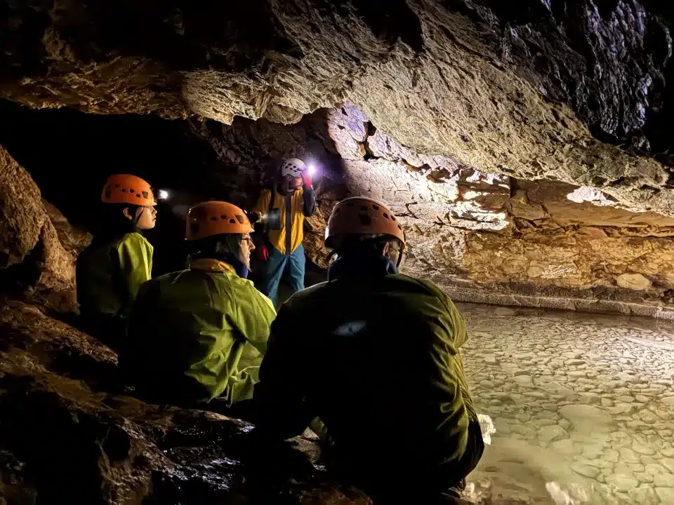 Des spéléologues équipés de casques et de lampes frontales observent une étendue d'eau claire dans une grotte du Dévoluy