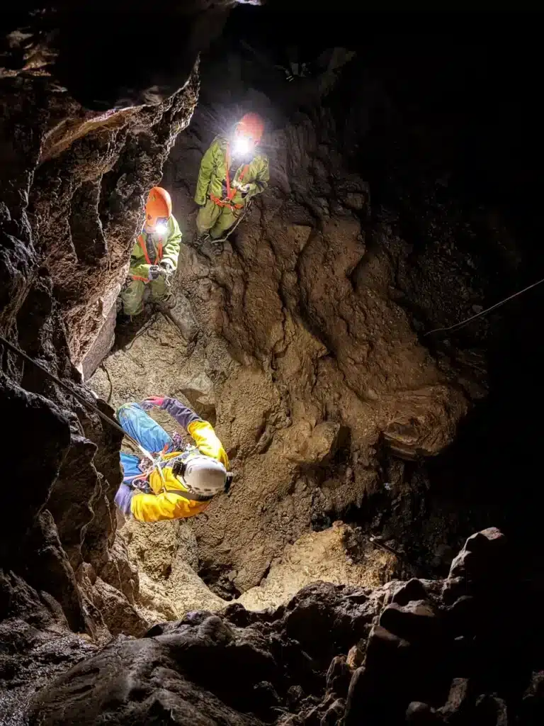 Trois spéléologues équipés de casques et de frontales descendent en rappel dans le gouffre du Chourum Camarguier