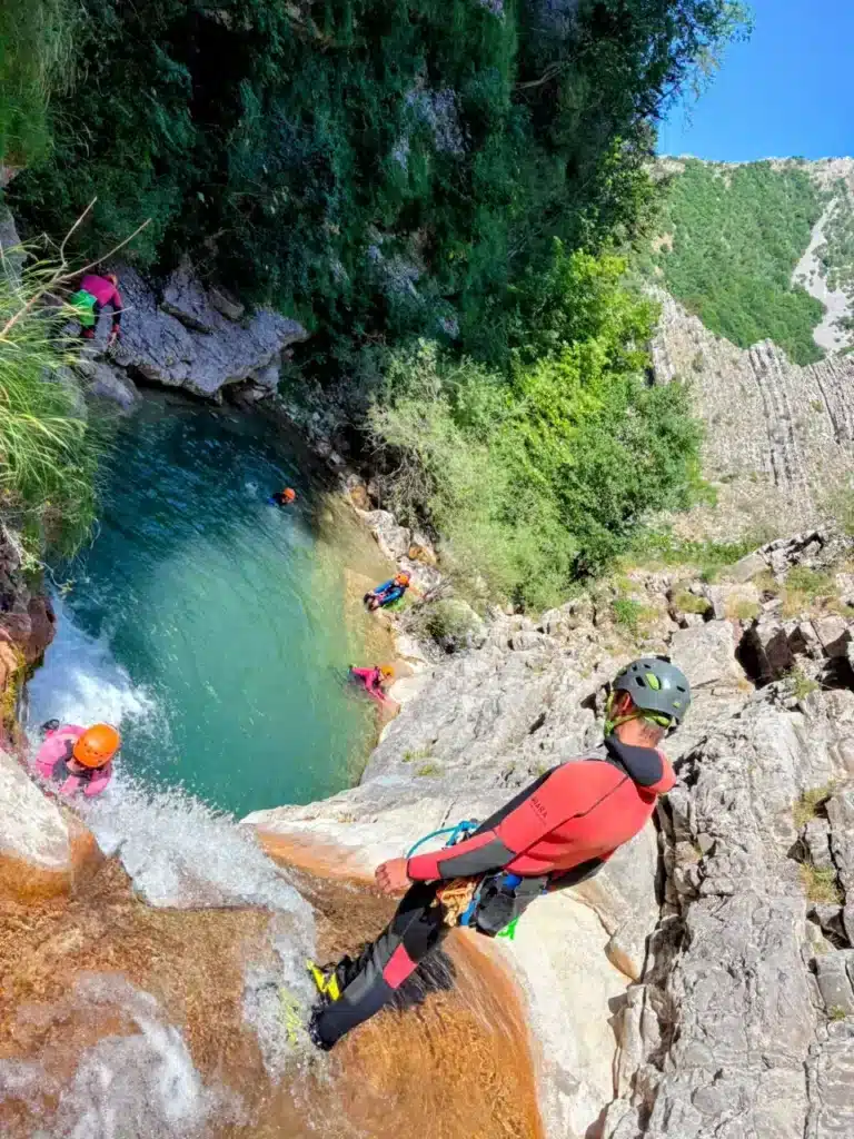 Un groupe de canyoneurs s'apprête à descendre un toboggan naturel à Rabou, certains nageant dans un bassin d'eau turquoise en contrebas.