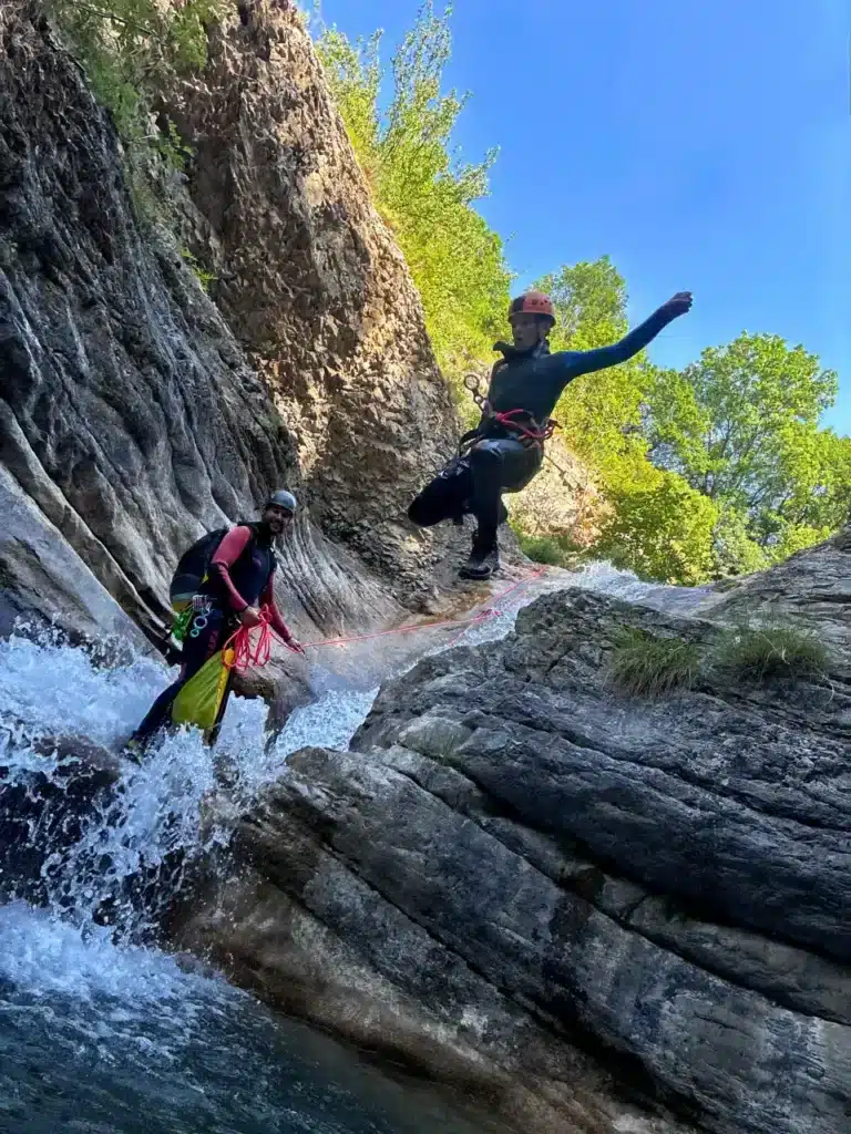 Deux personnes en combinaison néoprène, casque et cordes font du canyoning dans le canyon de Rabou.