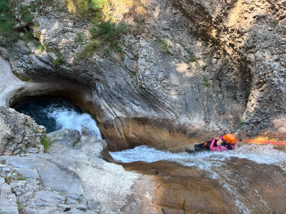 Une personne descend un toboggan naturel formé par la cascade de Rabou, portant un casque et une combinaison en néoprène.