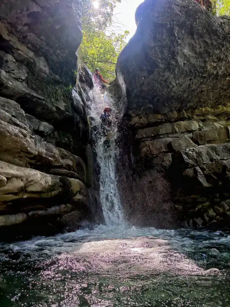 Deux personnes font du canyoning en descendant un toboggan naturel entre des falaises rocheuses à Rabou.