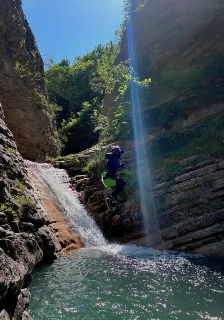 Une personne en tenue de canyoning saute d'une cascade rocailleuse dans une eau verte et tumultueuse dans le canyon de Rabou.