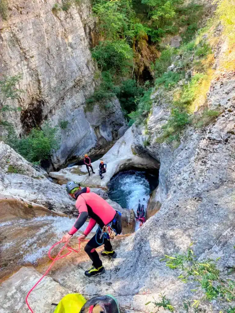 Un groupe de personnes fait du canyoning dans un canyon à Rabou, descendant en rappel une cascade vers un bassin d'eau turquoise.