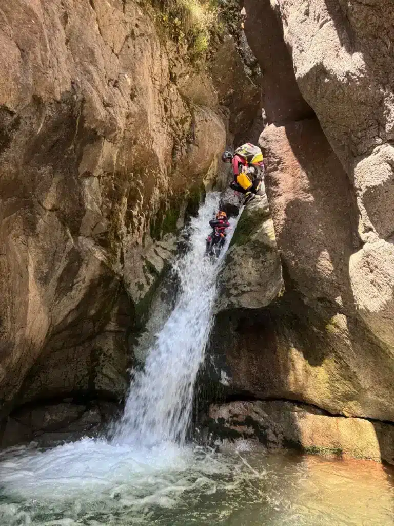 Deux personnes en équipement de canyoning descendent un toboggan naturel dans un canyon escarpé à Orcières Merlette.
