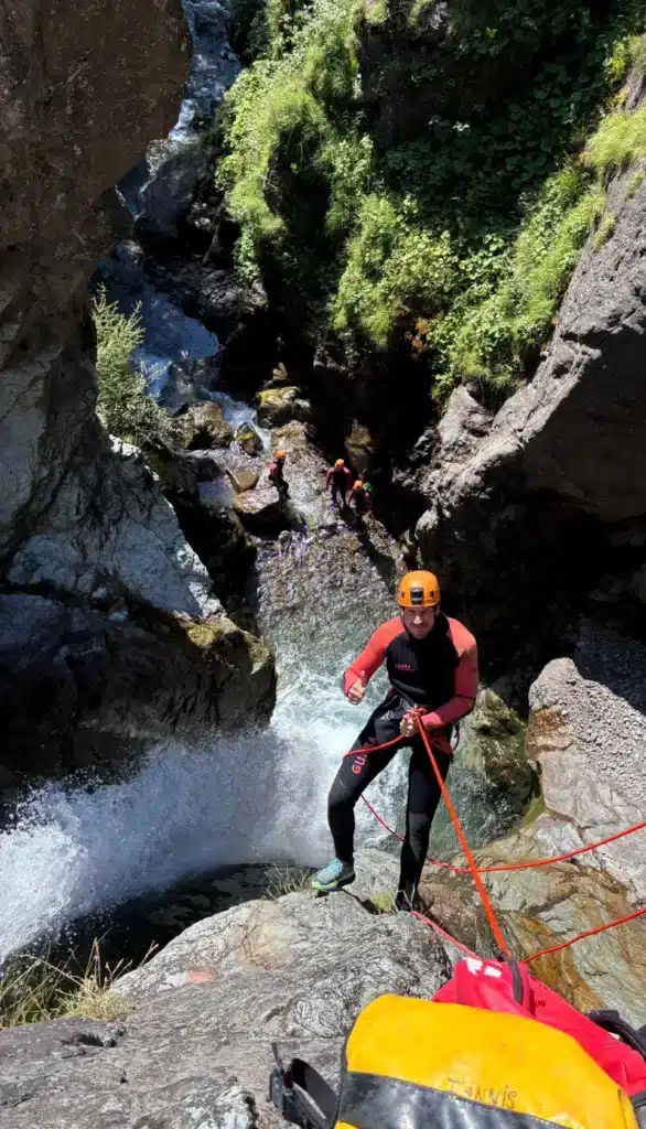 Un homme en tenue de canyoning avec casque descend en rappel une cascade entourée de rochers et de végétation dans le canyon de Val Estrèche à Orcières Merlette.