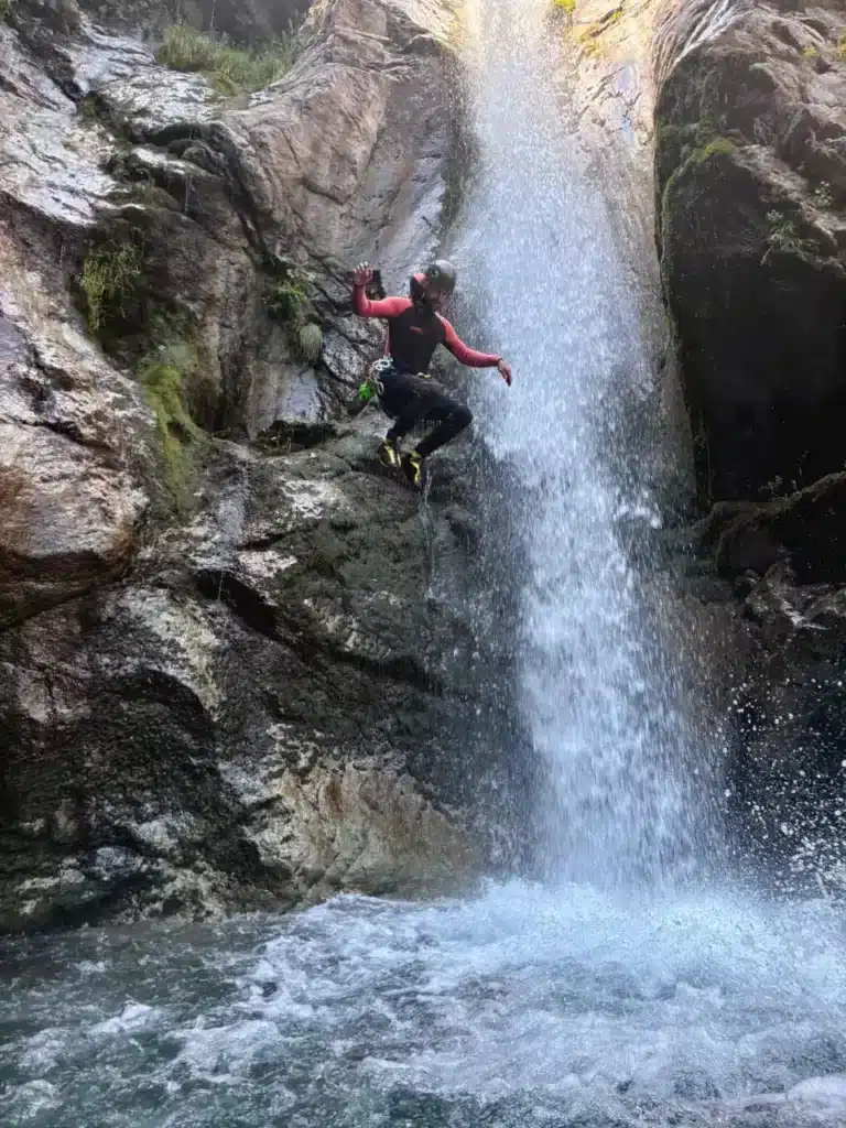 Un canyoniste en combinaison rouge et noire saute d'une falaise dans une cascade du canyon de Val Estrèche à Orcières Merlette.