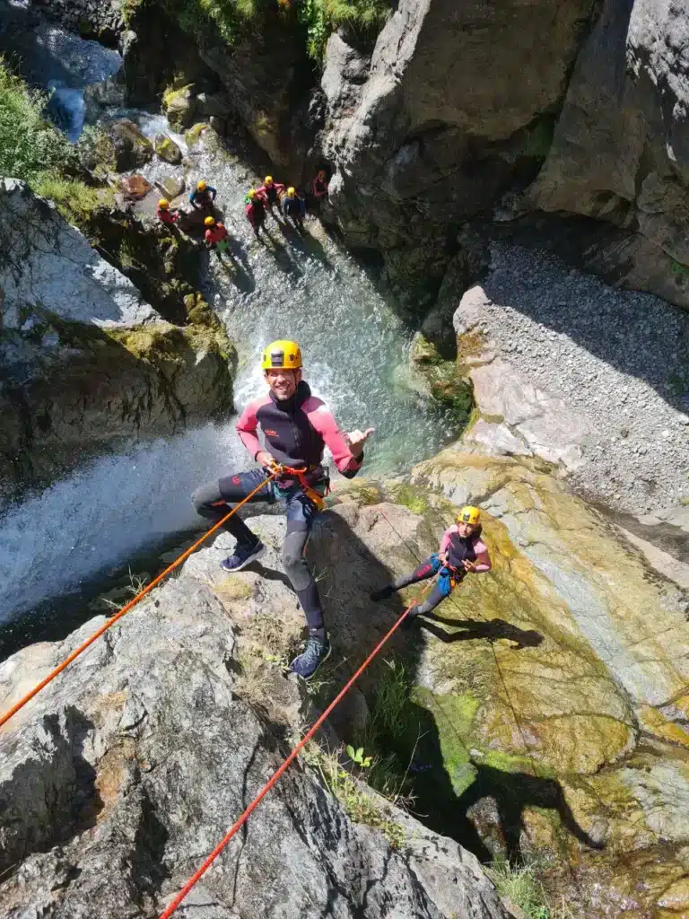 Deux personnes en combinaison et casque descendent en rappel une cascade dans un canyon à Orcières Merlette, avec d'autres personnes bas de la cascade.
