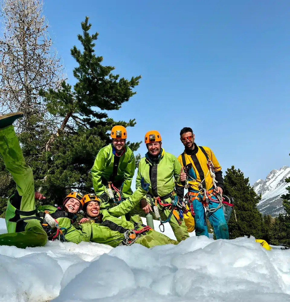 Cinq personnes souriantes en combinaison verte et casque orange, équipées pour la Via Souterrata de SuperDévoluy, posant dans la neige.