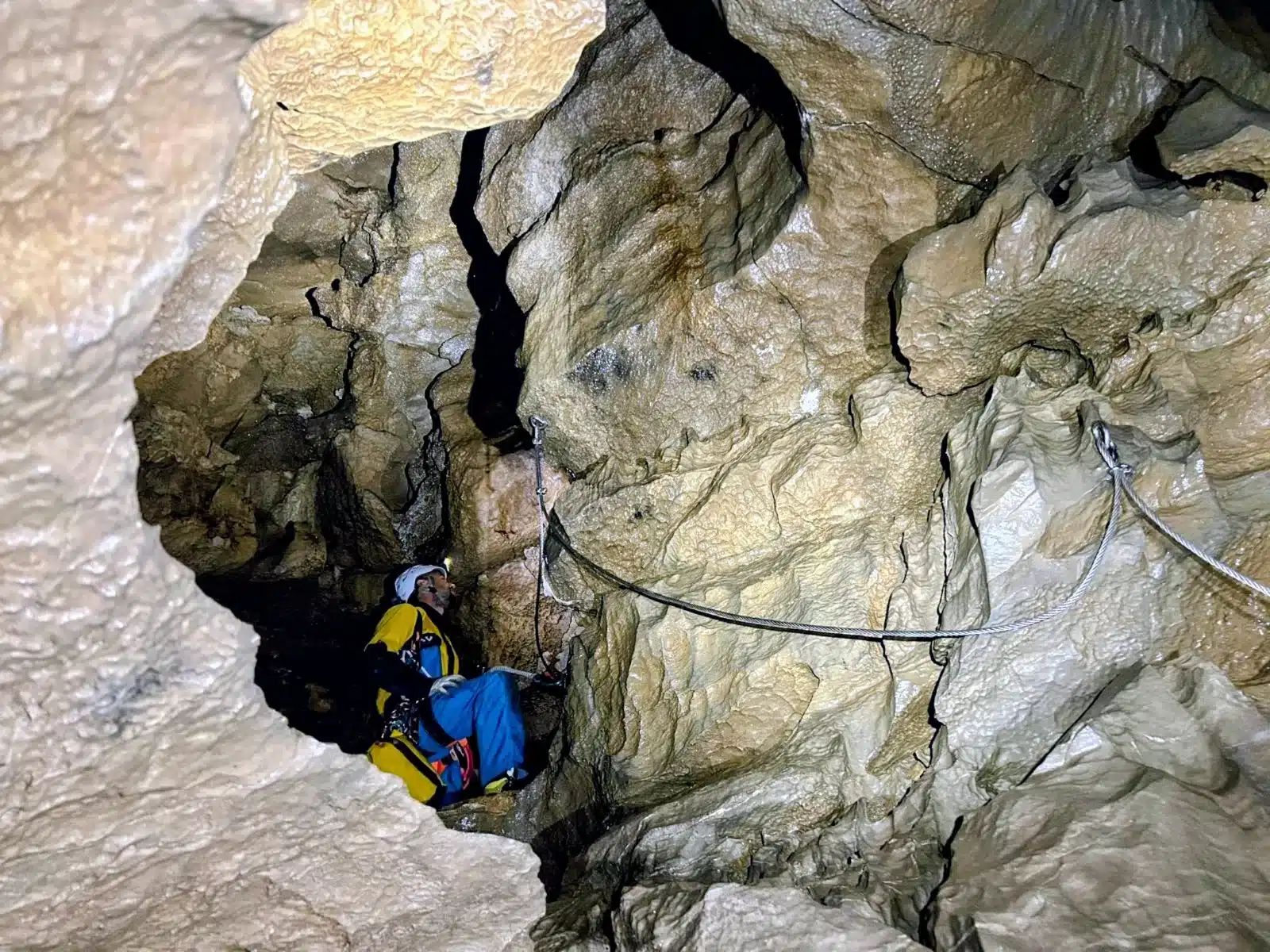 Spéléologue équipé d'un baudrier et d'un casque, assis dans une grotte, à côté d'une paroi de la viasouterrata de SuperDévoluy